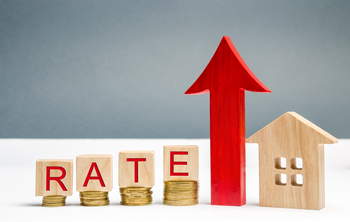 A home depicted with a rate sign and coins, representing the challenges of higher interest rates in the housing market.  