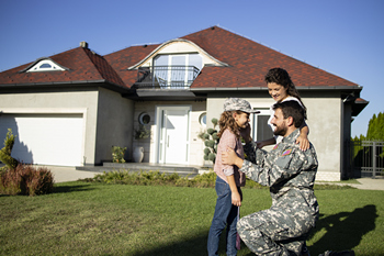 A soldier kneels in front of a house, smiling with two children, symbolizing family and homeownership through VA refinancing. 